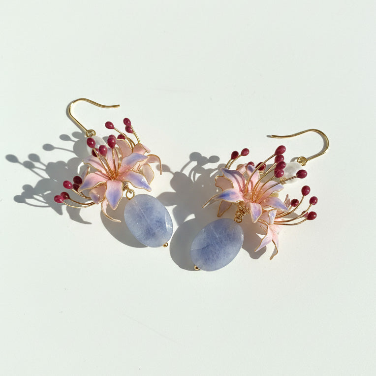 Pair of floral earrings with pink flowers and blue teardrop shapes on a light background