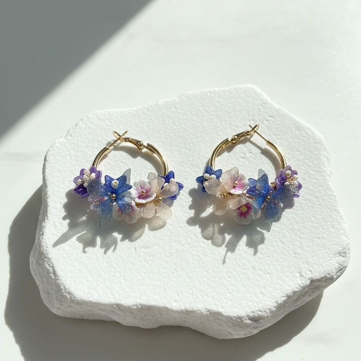 Blue and lilac flower hoop earrings with pearls displayed on stone base.