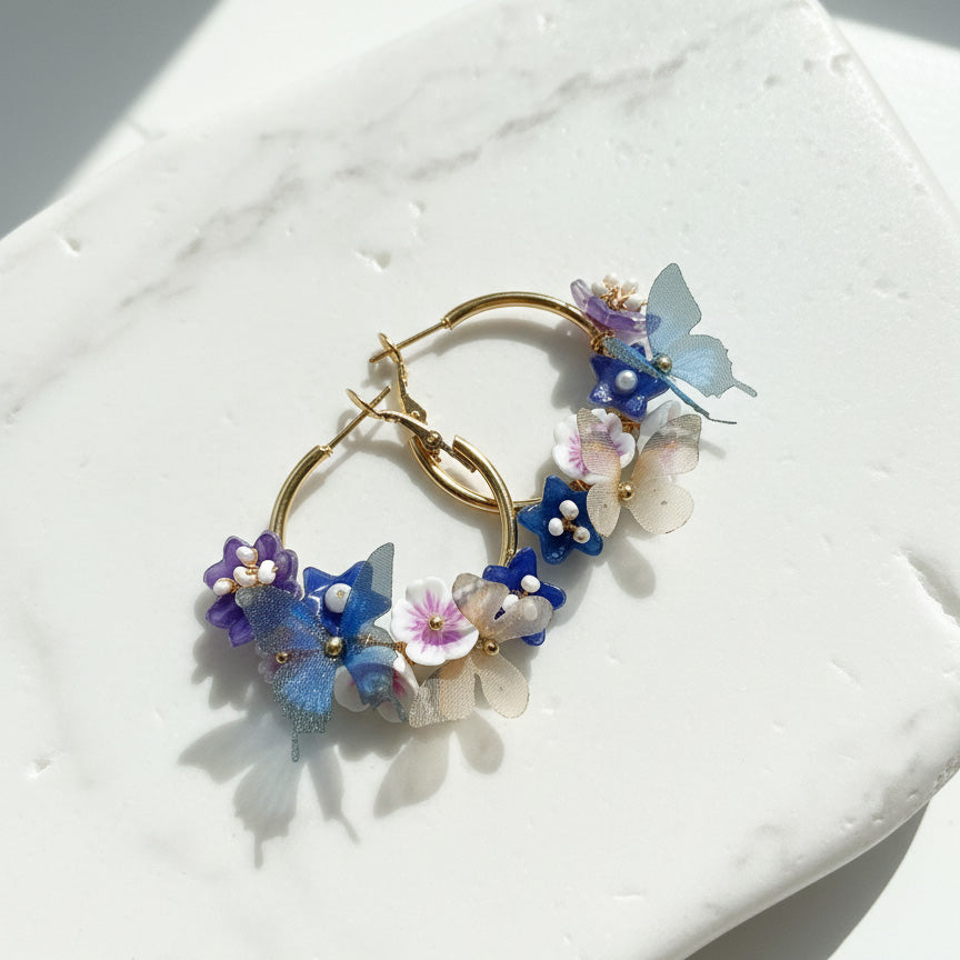 Gold hoop earrings with colorful floral and butterfly designs on a white surface