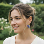 Model wearing floral hoop earrings with butterflies and pearls in garden setting.