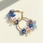 Handcrafted blue floral hoop earrings with butterflies and pearls on white background.