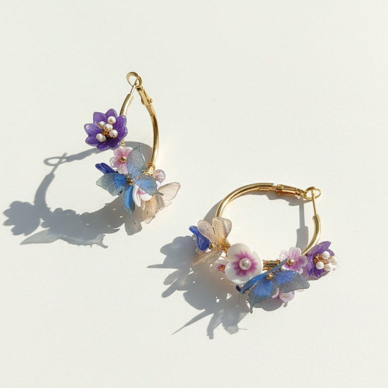 Gold hoops with hand-painted flowers and fabric butterflies in sunlight.