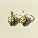 Pair of gold earrings with green and pearl accents on a beige background