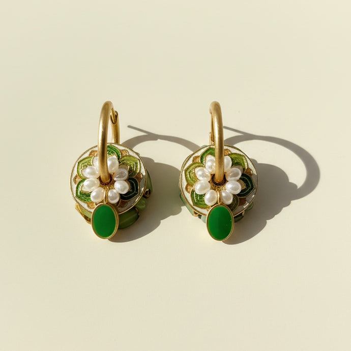 Pair of gold earrings with green and pearl accents on a beige background