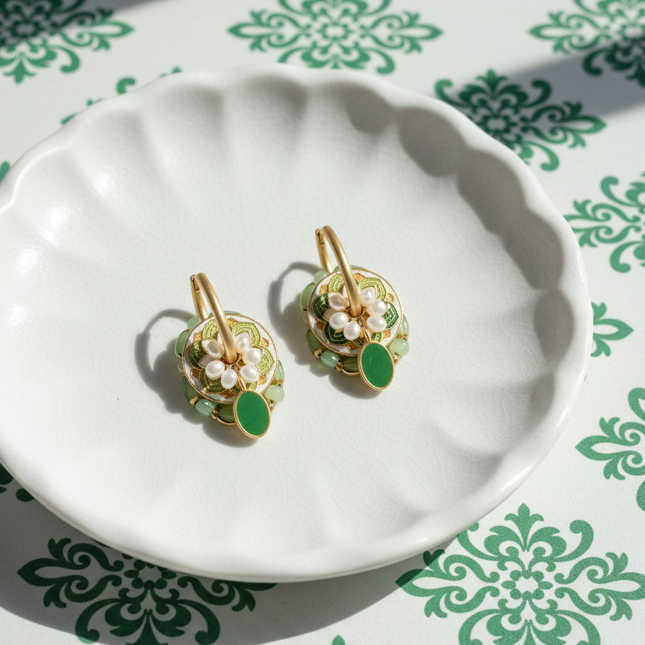 Close-up of green cloisonné floral earrings with pearls on white dish