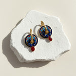 Pair of earrings with blue and red accents on a white stone surface