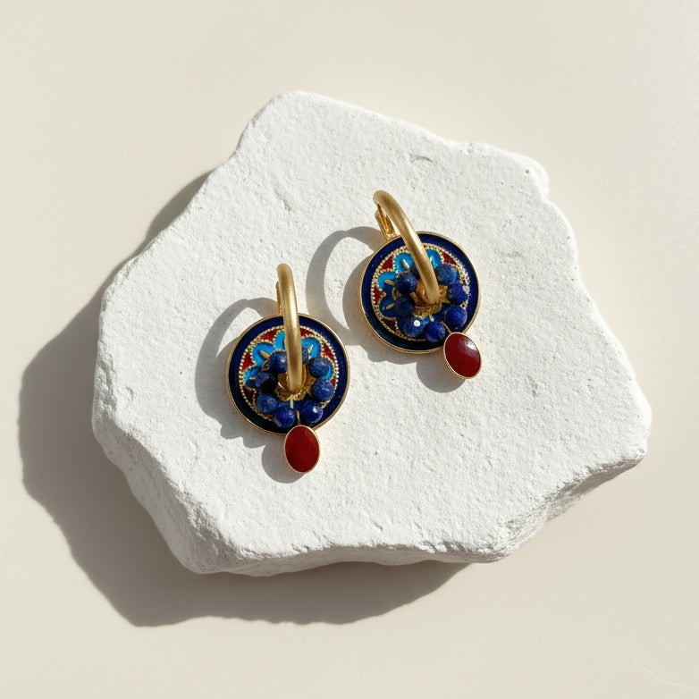 Pair of earrings with blue and red accents on a white stone surface