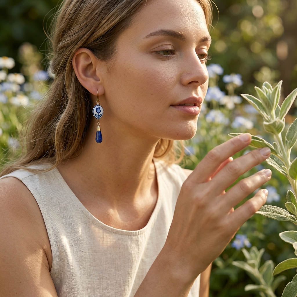 Woman wearing porcelain earrings holding a leaf in a garden with a blurred background