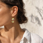Close-up of a woman wearing hand-painted porcelain beads with butterfly earrings with a neutral background