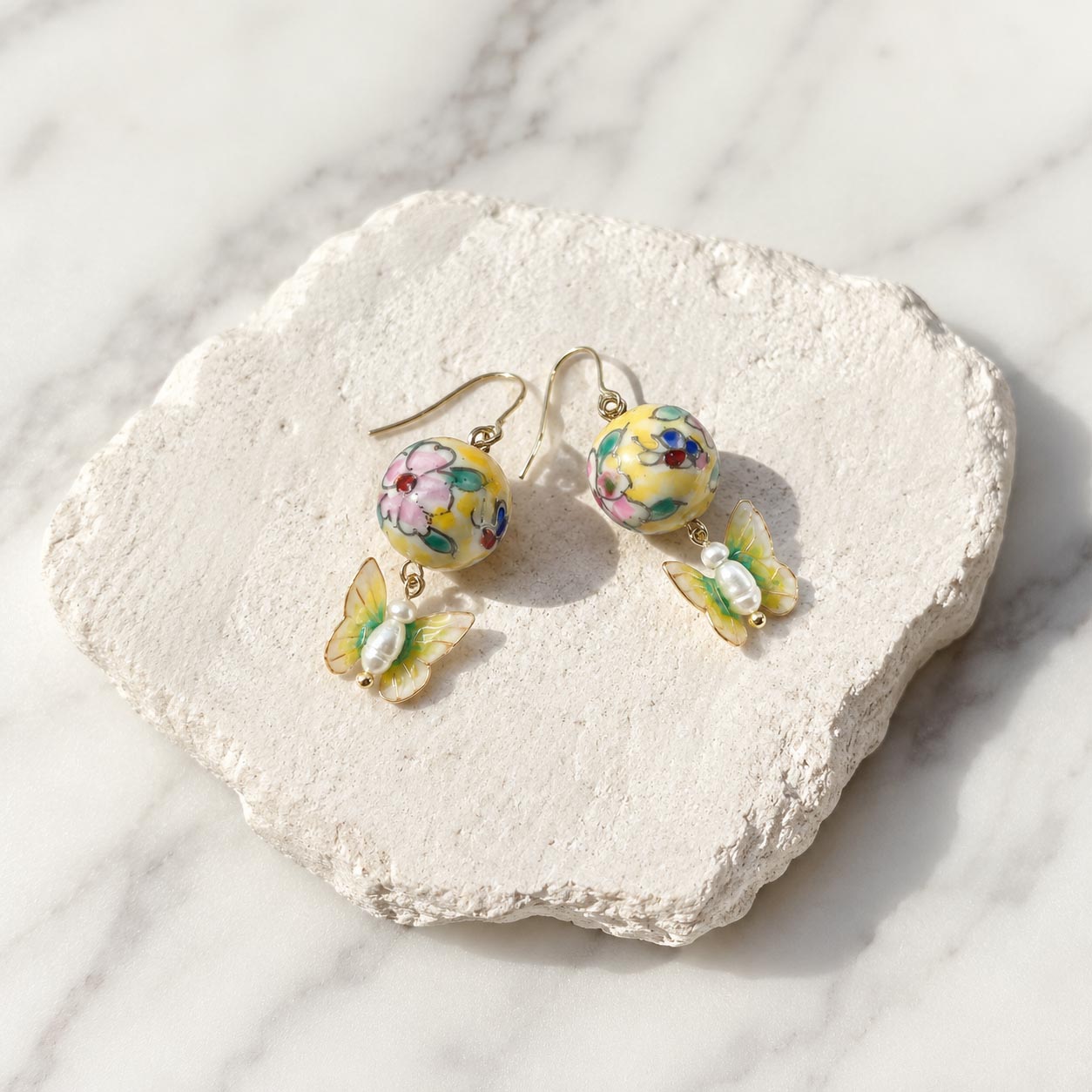 Butterfly Pearl Drop Earrings Featuring Hand-Painted Floral Porcelain Beads on a textured stone surface.