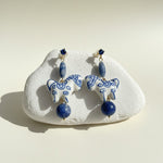 Pair of blue and white ceramic horse earrings on a white stone with a beige background