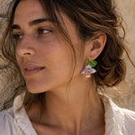 Woman wearing handcrafted purple orchid enamel stud earrings with sculpted green leaves and botanical floral design.