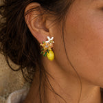 Close-up of hand-painted lemon blossom stud earrings featuring enamel flowers, handcrafted resin blossoms, green leaves and lemon charms.