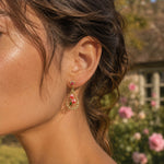 Close-up of a woman's ear wearing pink bell flower earrings with a garden background
