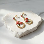Gold earrings with floral designs on a white stone surface