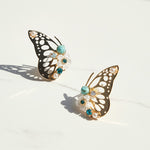 Gold butterfly earrings with turquoise stones, pearls, and floral accents on white background.