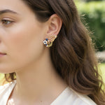 Gold butterfly earrings with blue gemstones, pearls, and floral accents worn by woman outdoors.