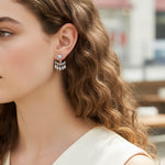 Close-up of a woman wearing a silver earring with a central gemstone and dangling elements.