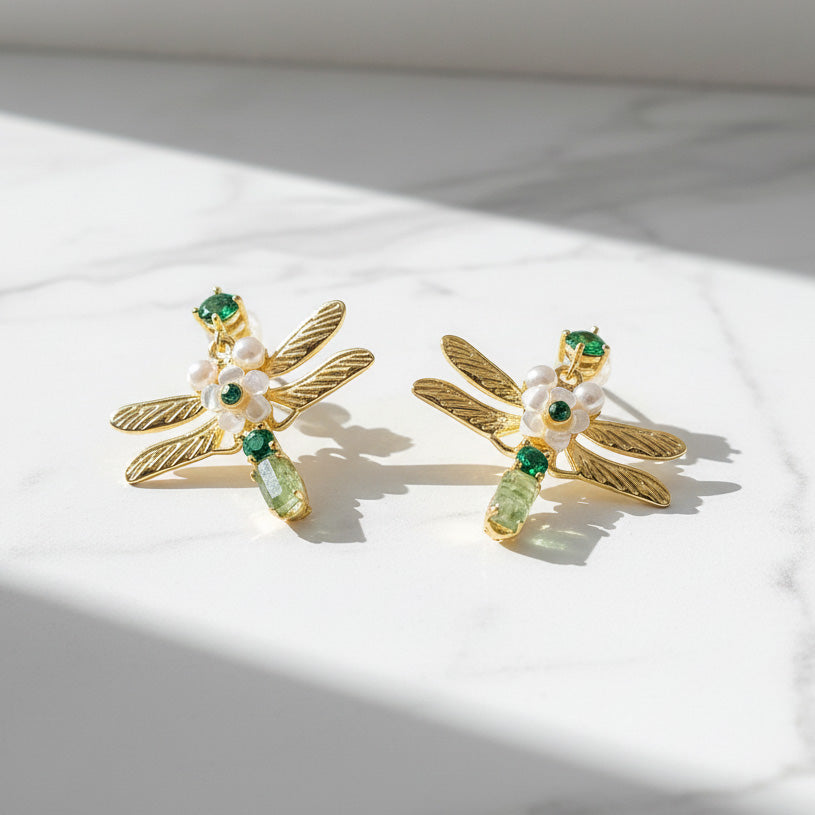 Dragonfly-shaped earrings with green and pearl details on a light background