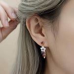 Close-up of an ear wearing a floral earring with colorful stones.