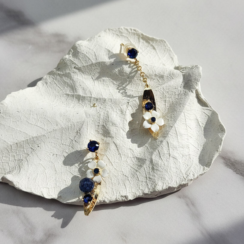 Gold earrings with blue gemstones on a white leaf