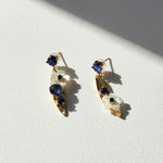 Pair of gold earrings with blue gemstones and white floral elements on a light background