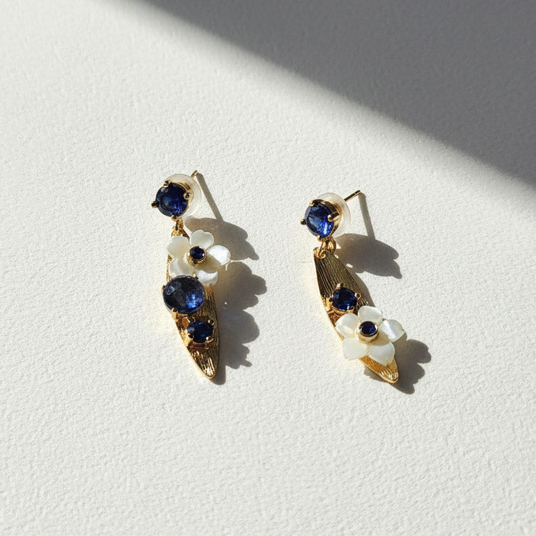Pair of gold earrings with blue gemstones and white floral elements on a light background