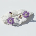 Purple flower-shaped earrings on a white shell against a white background