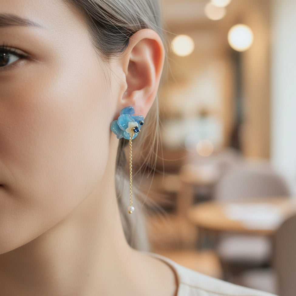 Close-up of a woman wearing a blue floral earring in an indoor setting.