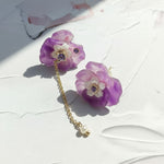 Purple floral earrings with a gold chain and pearl on a white surface
