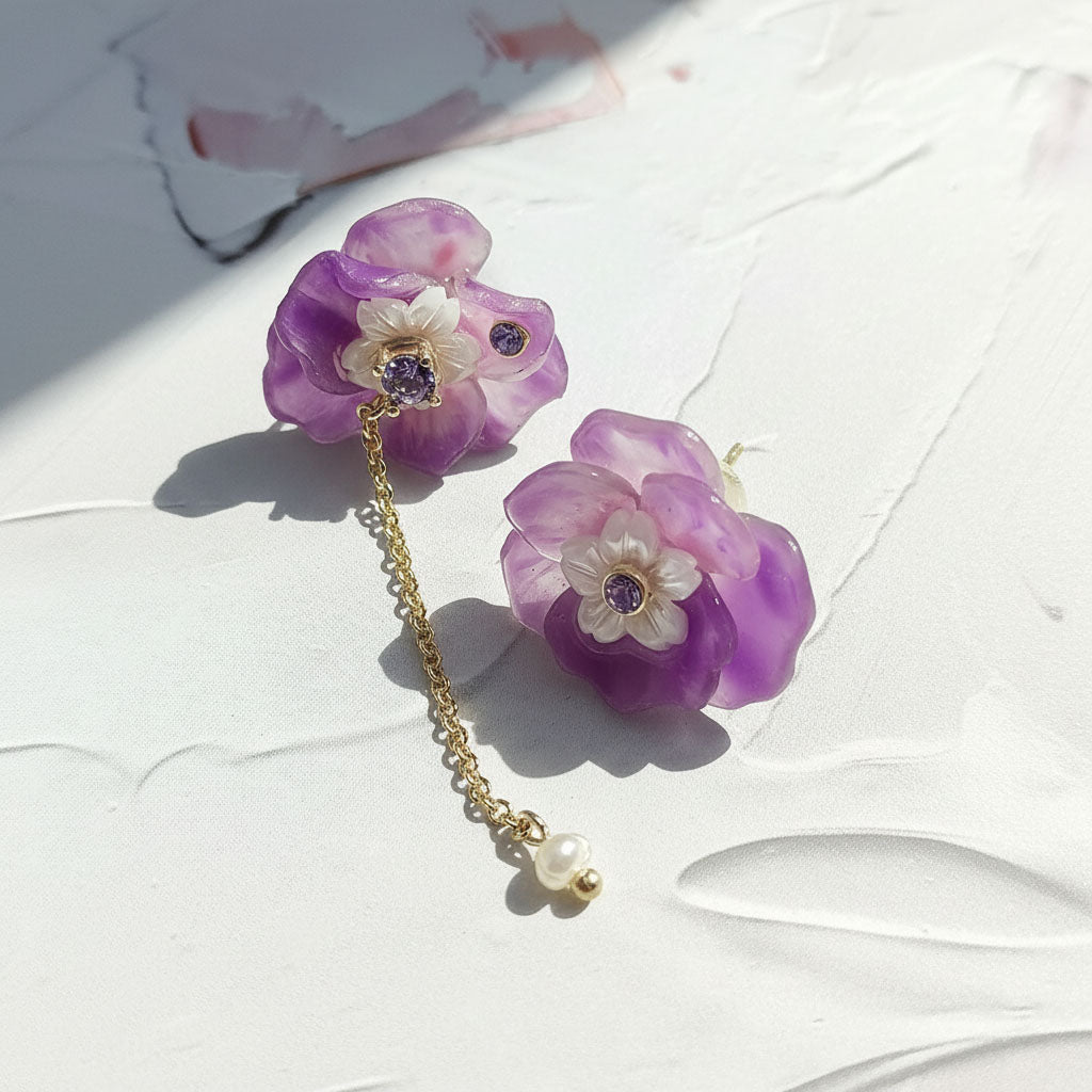 Purple floral earrings with a gold chain and pearl on a white surface