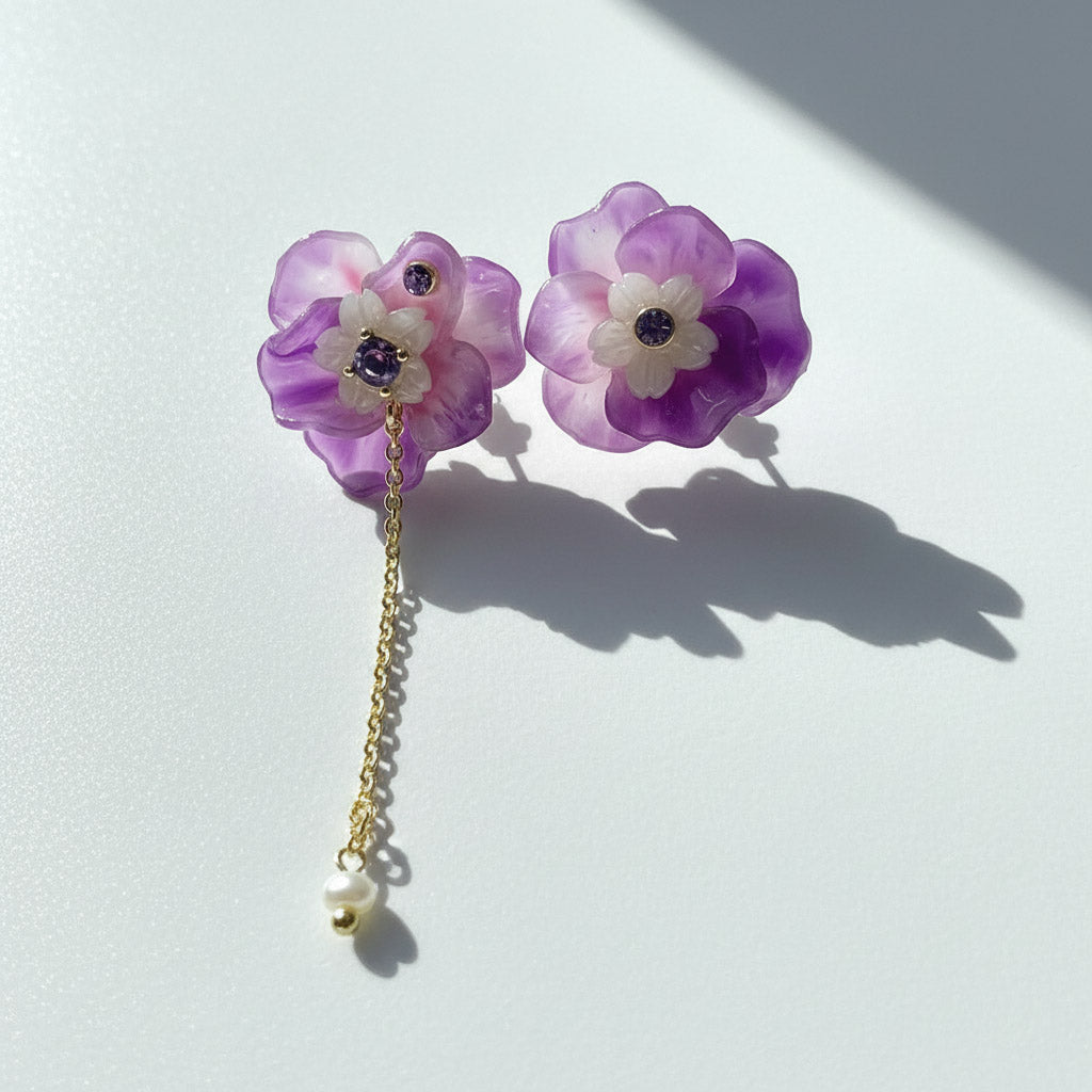 Purple floral earrings with a gold chain on a white background