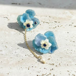 Pair of blue floral earrings with white flowers and gold chain on a light surface