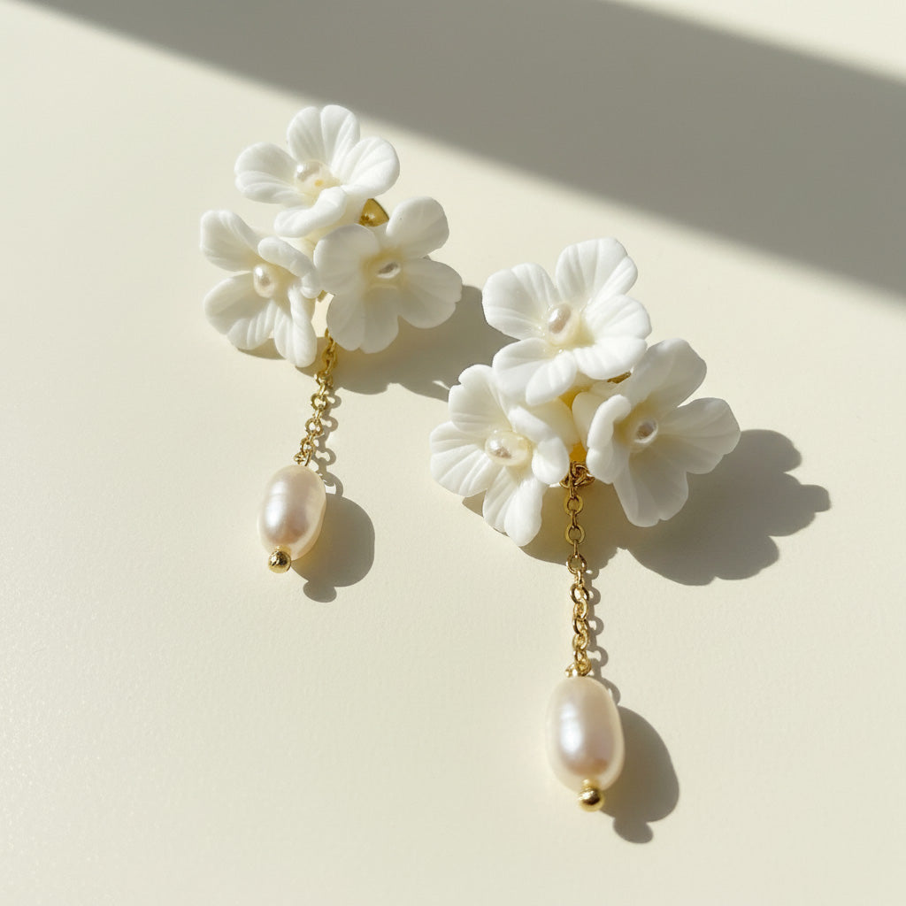 Porcelain blossom and pearl drop earrings on cream background with sunlight and shadow.
