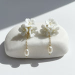 Close-up of white porcelain flower earrings with gold chain and pearl drop.