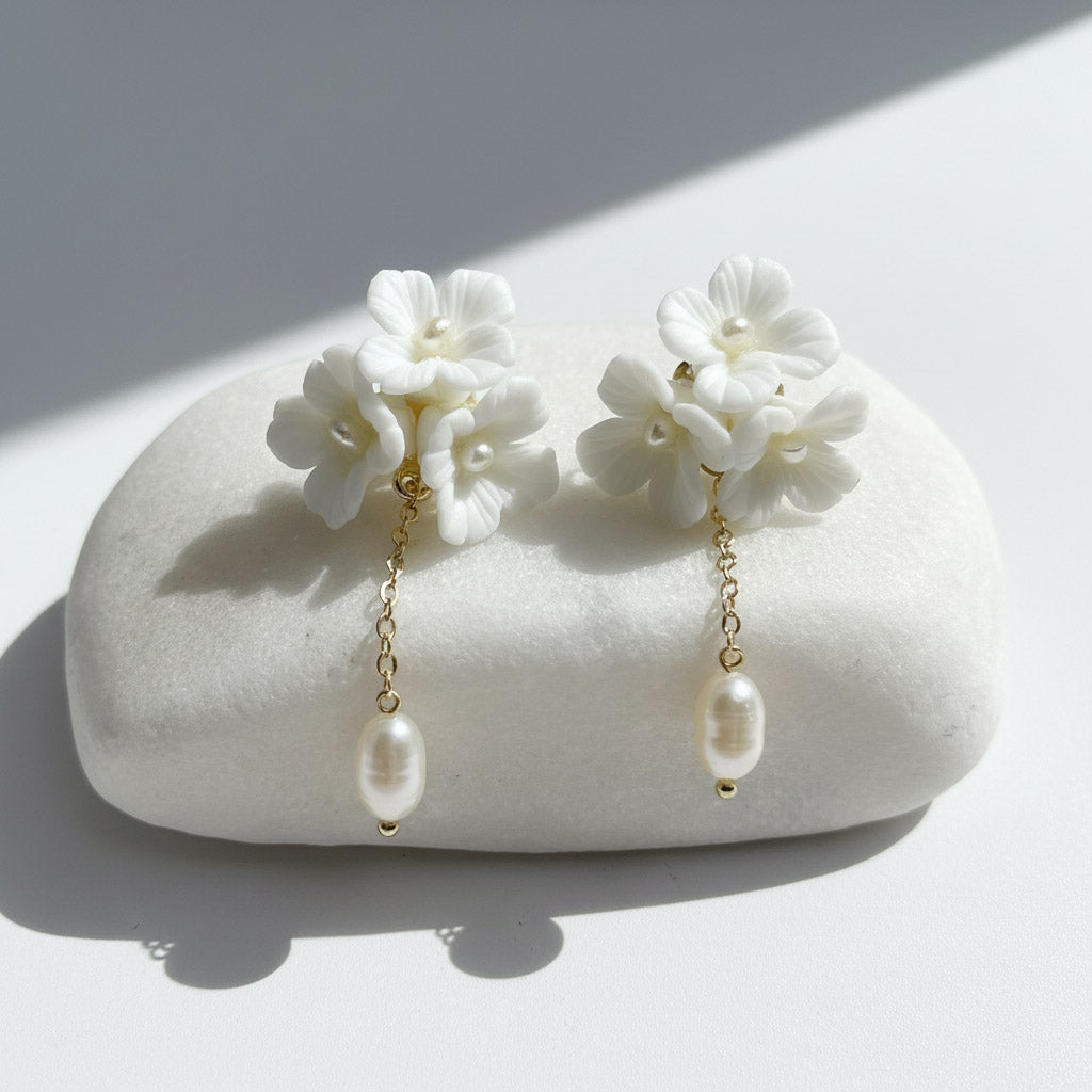 Close-up of white porcelain flower earrings with gold chain and pearl drop.
