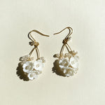 Pair of gold earrings with white floral designs on a light beige background
