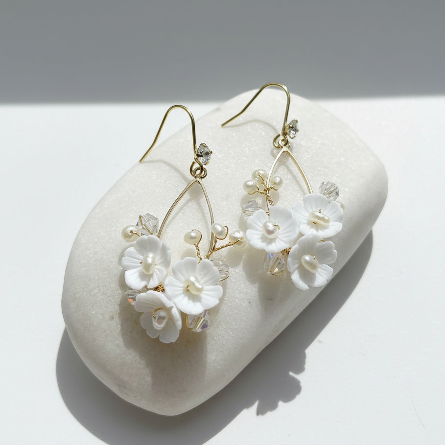 Pair of floral earrings with white flowers and gold accents on a light background