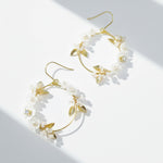 Gold hoop earrings with white floral and leaf details on a light background