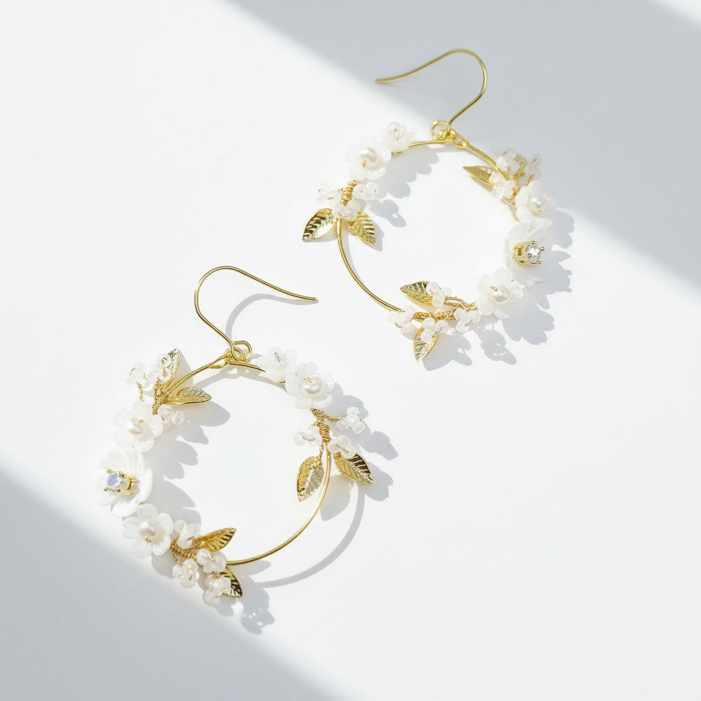 Gold hoop earrings with white floral and leaf details on a light background