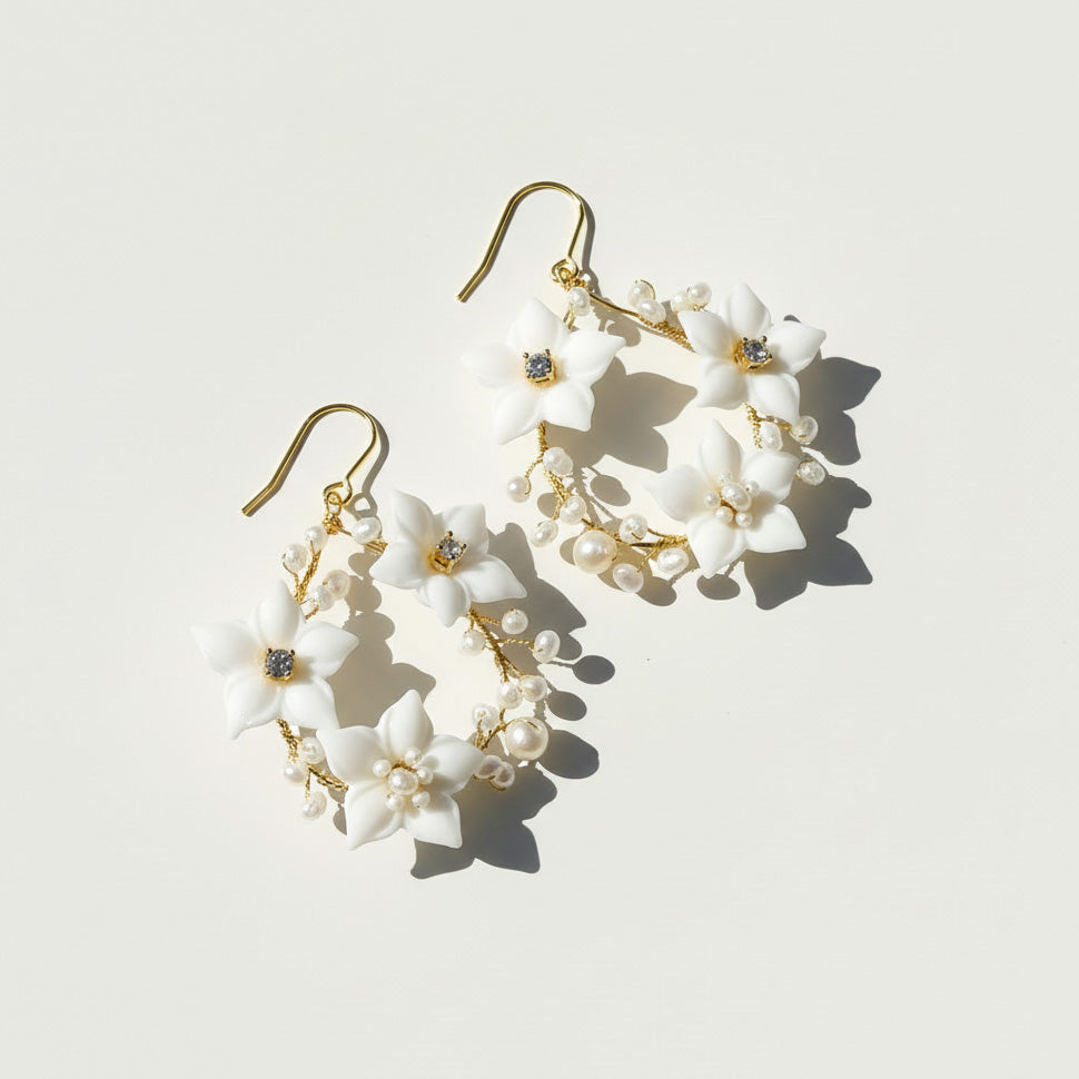 Pair of floral earrings with white flowers and gold accents on a light background