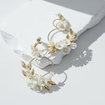 White floral and pearl statement hoop earrings with gold leaves on neutral background, sunlight and shadow.