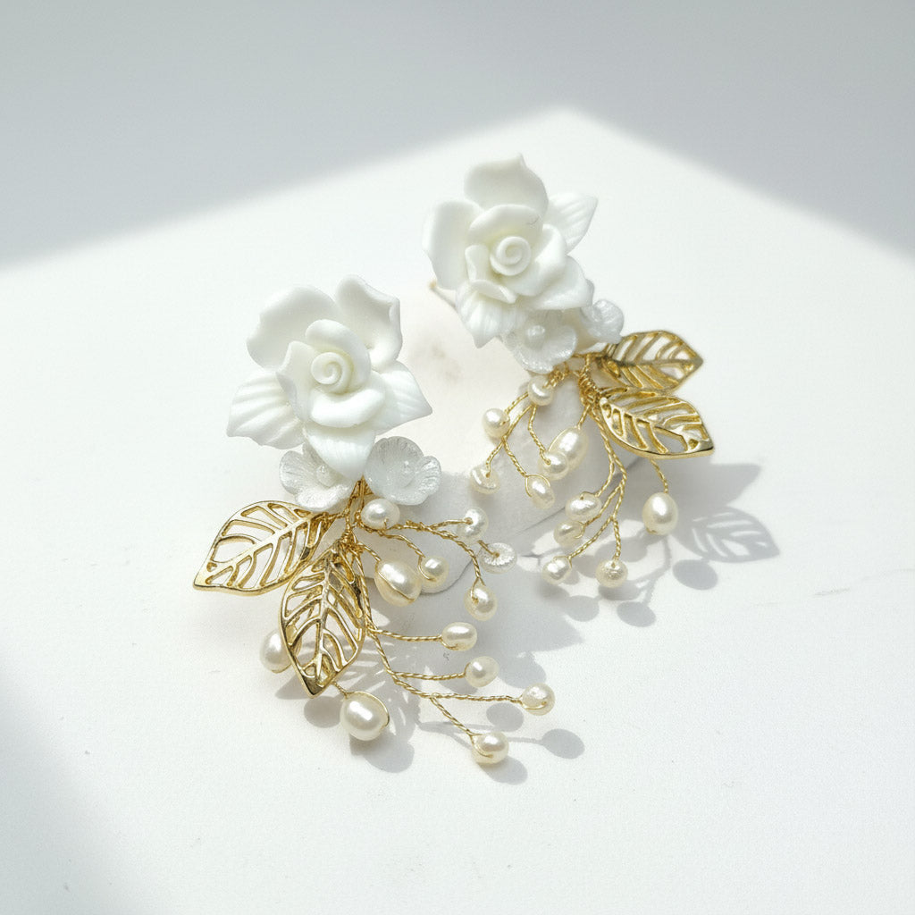 Pair of floral earrings with gold leaves and pearls on a white background