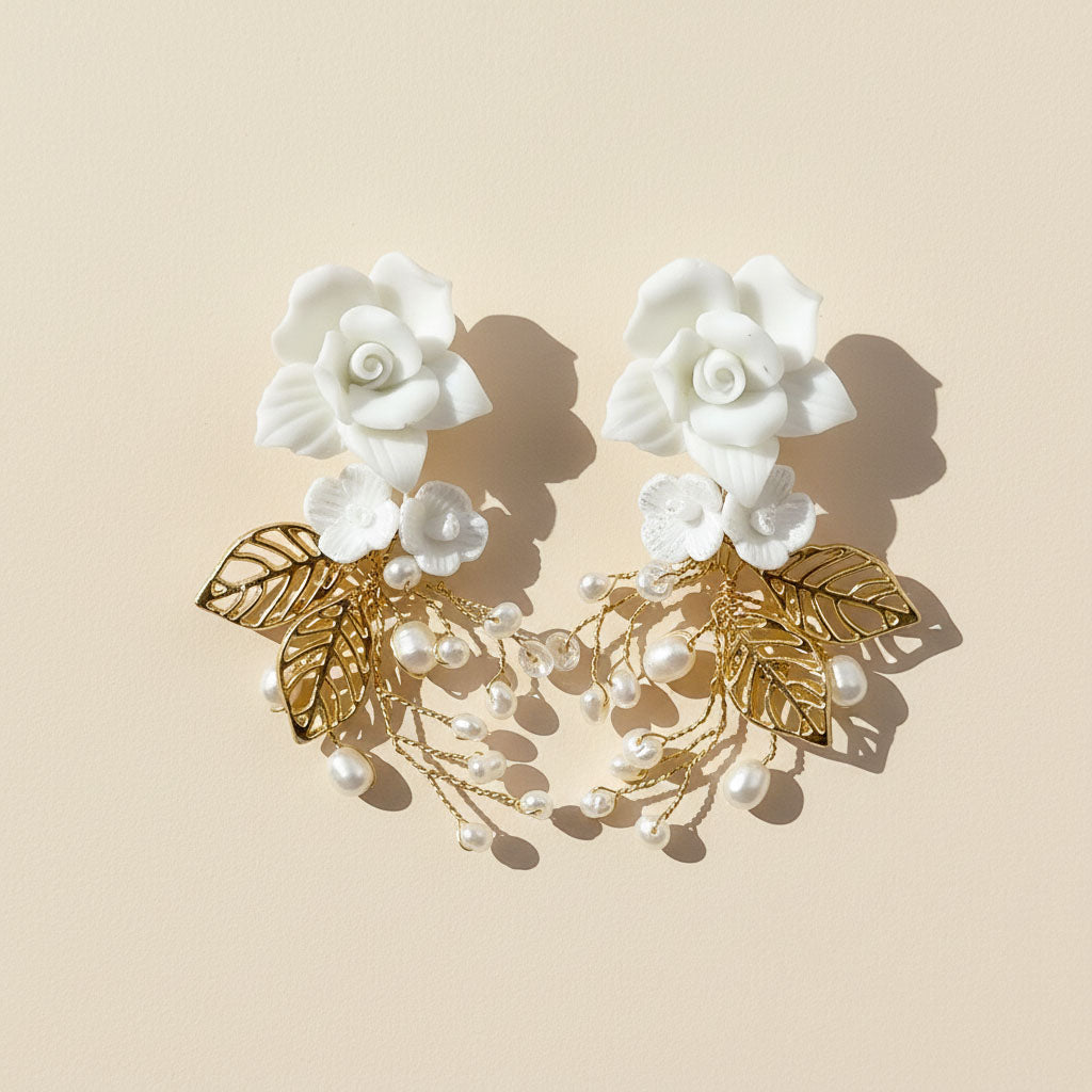 Pair of floral earrings with gold leaves and pearls on a beige background