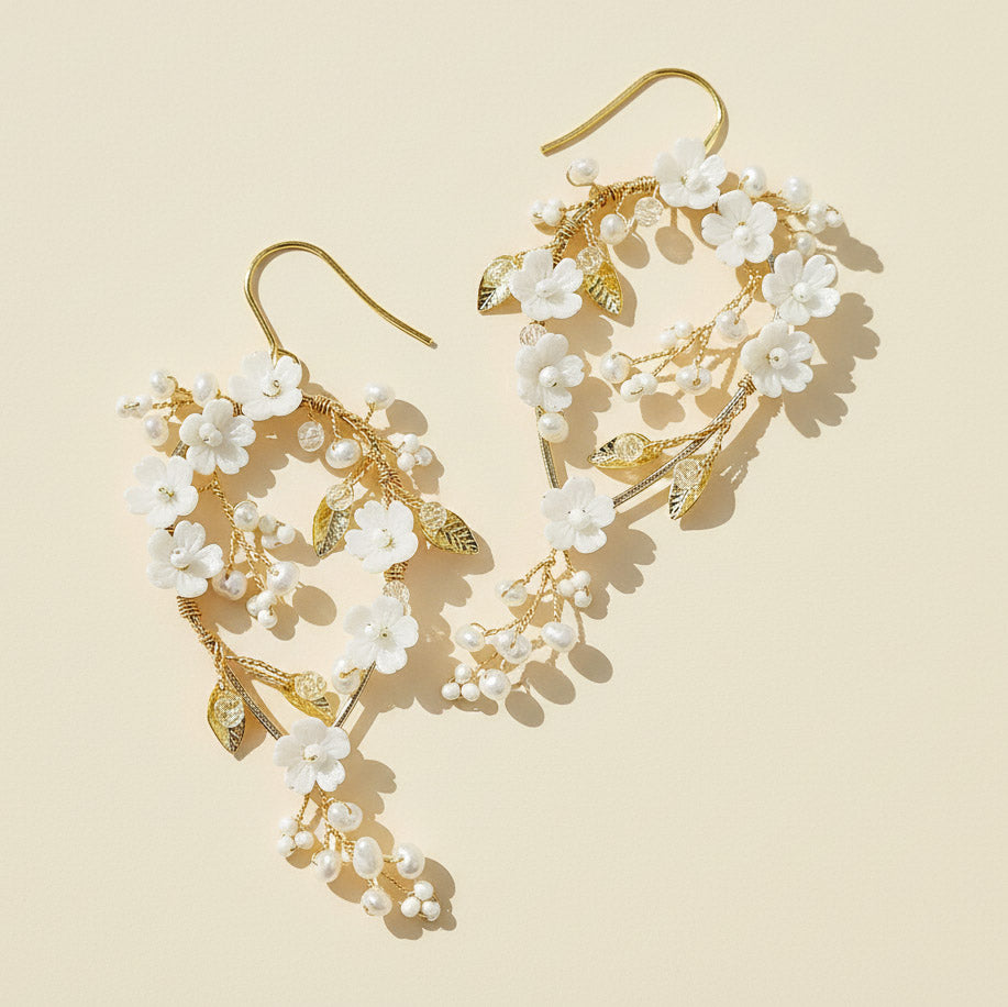 Gold and white floral earrings on a beige background