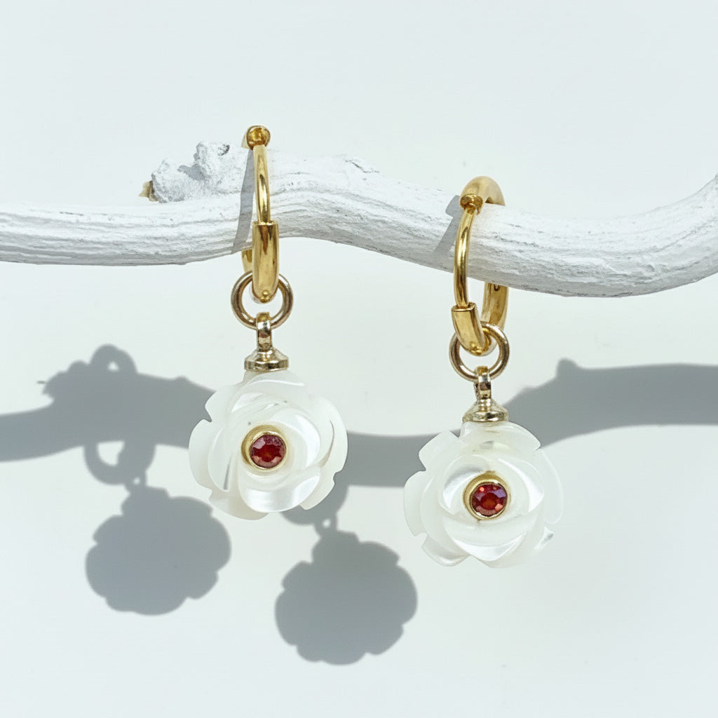 Pair of earrings with white floral designs and red gemstones on a light background