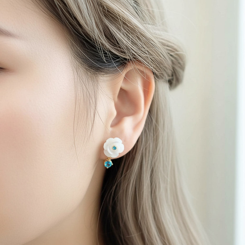 Close-up of an ear wearing a floral earring with a blue gemstone against a neutral background