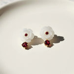 Pair of earrings with white floral designs and red gemstones on a light background