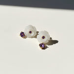 Pair of white floral earrings with purple gemstones on a light background