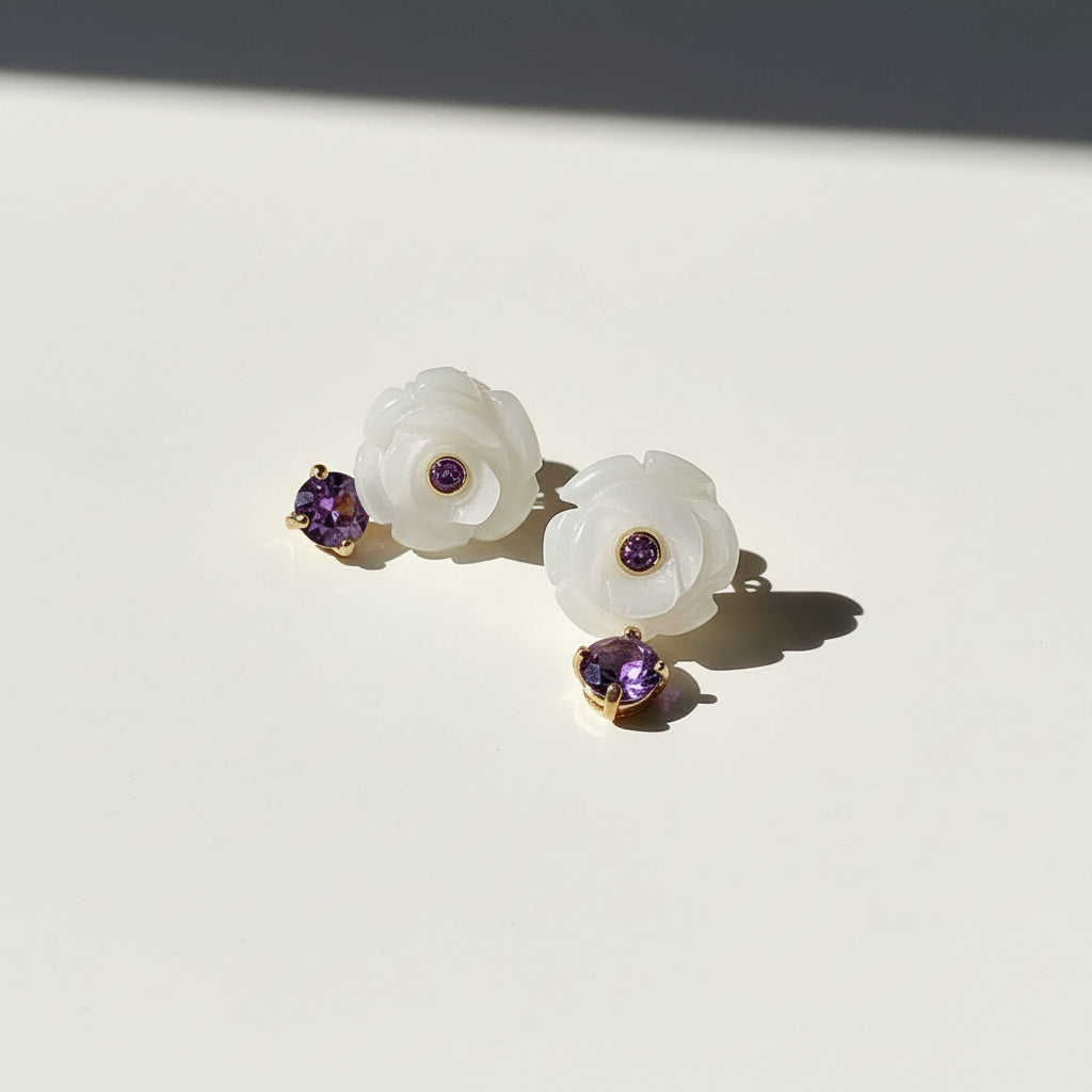 Pair of white floral earrings with purple gemstones on a light background